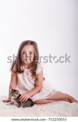 little girl with long hair in a studio on a white background sitting down playing with a kitten

