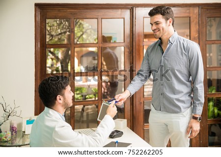 Attractive young man using a credit card to pay for some health services in a wellness and spa clinic