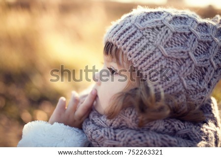 Autumn outdoor portrait of happy child girl, wearing warm white coat, scarf and hat, toned photo