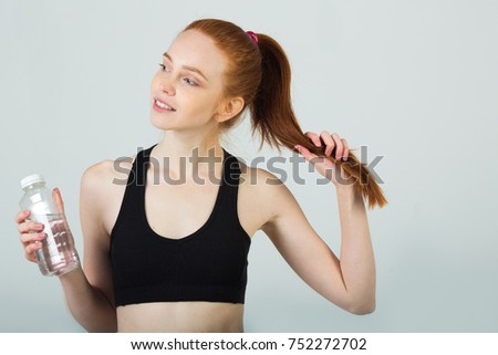 beautiful slender girl with red hair in sportswear on a light background with a bottle of water