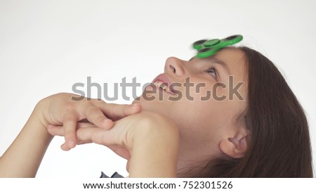 Beautiful cheerful teen girl spinning a green fidget spinner on her forehead on a white background