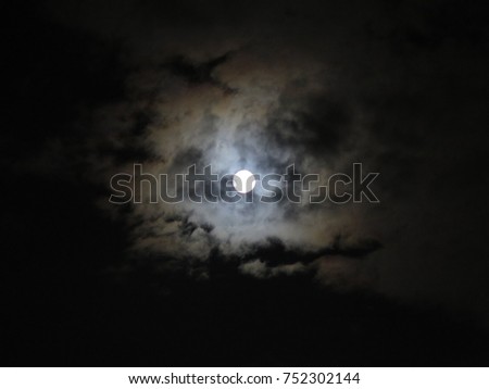 Moon poking out from behind clouds, scary night in Halloween festival concept, dark sky with cloudy around full moon in the middle of picture, space or background in nightmare or cant sleep content  
