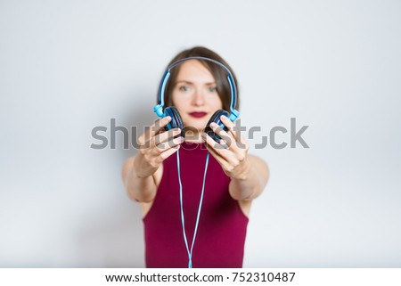 beautiful young woman listening to music with headphones, wearing a burgundy dress, isolated in studio on a gray background