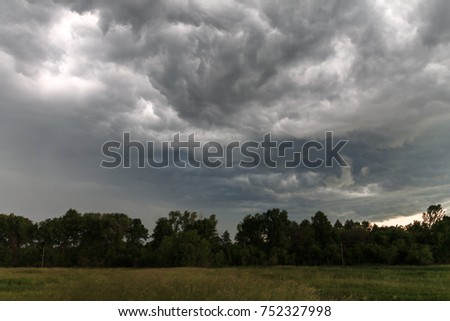 A thundercloud over a field in the countryside. Rain on a summer day. Beautiful clouds in the blue sky. Before the heavy rain. Field of meadow grasses. Black cloud.
