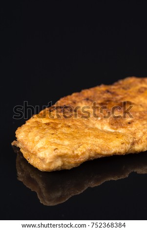 Fried breaded chicken white meat breasts in eggs above black background table with reflections and copy space.