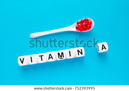 Red capsules in the white spoon and word vitamin A from white cubes with letters on blue background. healthy and medical concept. retinol, retinoic acid,  provitamin A, carotenoid, Beta-Carotin Royalty-Free Stock Photo #752393995