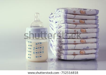 Baby bottle with milk and diapers on reflected background