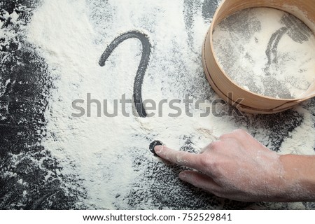 A woman's hand draws a question mark on flour. Sieve for flour and the concept of homemade cakes.