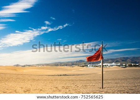 red flag on sand in desert with mountains and blue sky on background /red flag on the beach