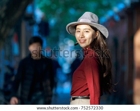 Pretty Chinese young woman stand in warm sunshine and looking back in street.