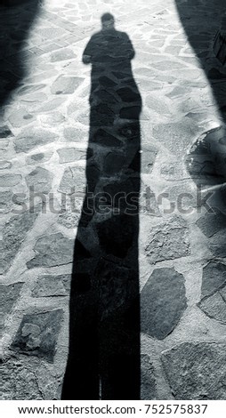 Shadow of a man on a crazy paving stone floor with buildings. Monochrome picture