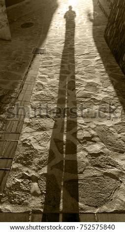 Shadow of a man on a crazy paving stone floor with buildings. Monochrome picture