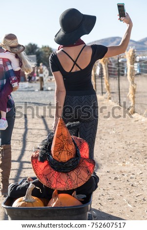 Mother Taking Selfie Picture Pulling Child In Wagon At Pumpkin Patch During Fall Holiday Season. Vertical Orientation.