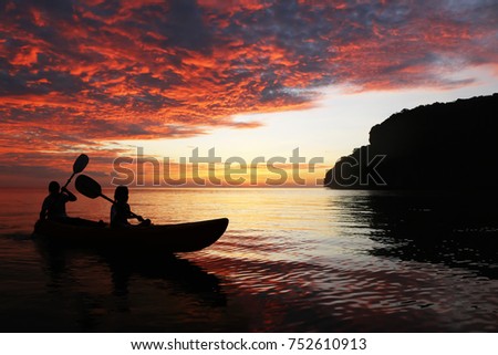Silhouette mother and daughter  kayaking in the ocean around the island with beautiful red sky sunset in Thailand.
