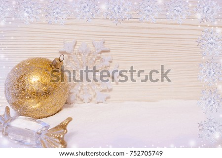 Christmas card. Two rows of snowflakes, golden Christmas decorations ball, candy and snowflake are lying on snow, light colored wooden background and copy space.