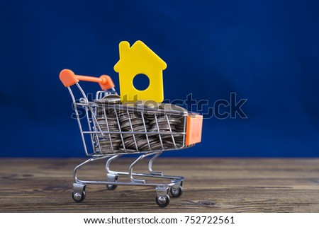 Concept of a yellow house in a shopping trolley on a blue background. Idea: buying a house, renting, selling real estate. Mortgage. Loan for housing.