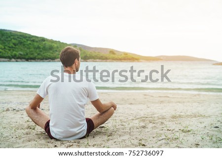 Young man meditating on beach in lotus position. Toned picture, Copy space.