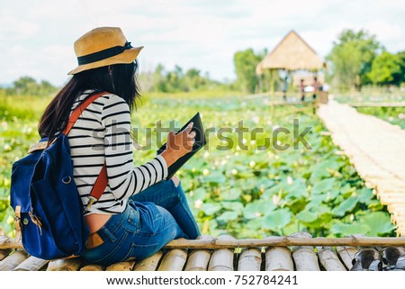 woman traveler siting and reading a book on the wood bridge and looking for beautiful lotus pond.Asia lady tourist enjoying on her vacation.