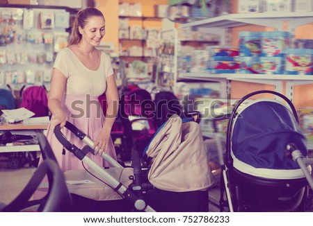 Cheerful smiling pregnant woman buying baby stroller in kids mall