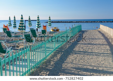 green fence dividing the public beach from the private, with deckchairs and beach umbrella, Mediterranean Sea, Italy