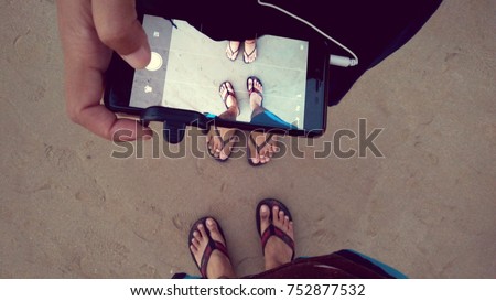 Couple taking picture of their feet on the Guhagar beach sand using mobile camera in India with retro / vintage filter effect
