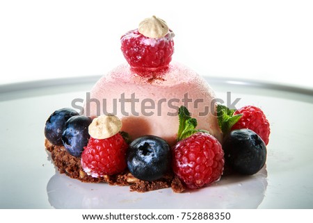 delicious pink dessert covered with fresh raspberries and blueberries on a white plate against white background