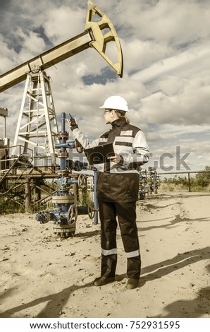 Woman engineer in the oilfield talking on the radio wearing white helmet and work clothes. 