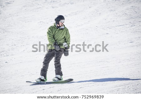 Male adult snowboarder riding down a groomed snow hill. A beautiful day on the slopes having fun
