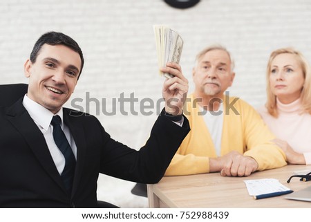 Mature couple at a reception with a lawyer. The lawyer holds a bundle of money and smiles. Old people sit next to him and look at him. They are sitting at the desk in the lawyer's office.