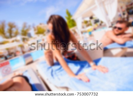 Blurred for background. Men and women sunbathe on sun lounger by pool. Boy and girl take solar bathrooms in luxury beachfront complex of luxury. Day holiday on beach lounge party.
