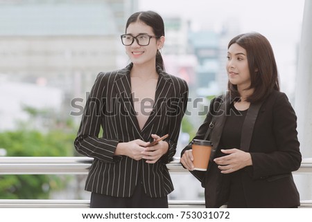 Two beautiful confident asian business woman taking a coffee break during break time. Two women in office suits talking during office break time, taken outdoor in natural light. Career woman concept.