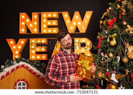 The guy is holding a Christmas gift and is standing by the tree. Merry Christmas and Happy New Year.