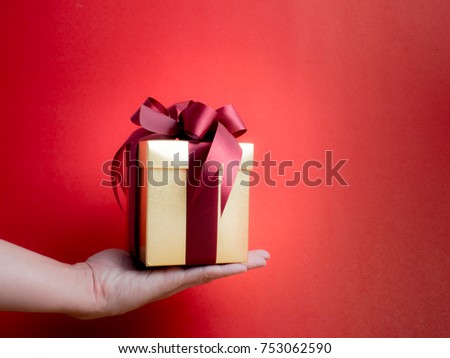 Valentine festival , New year Gold gift box with red ribbon. Red background for create idea copy space.hand holding gift box