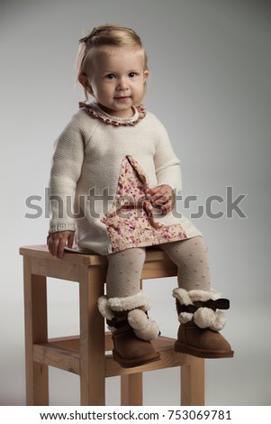 full body picture of a little girl smiling and sitting on chair wearing knitted dress and furry boots
