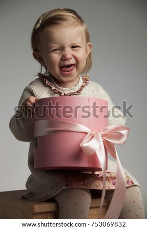 super excited little girl screaming while holding a round pink box, studio picture