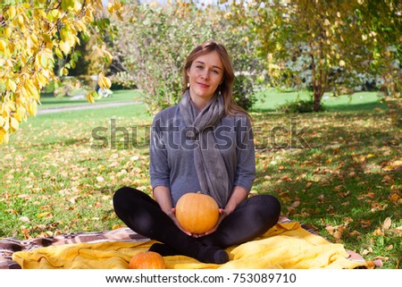 Cute happy pregnant woman on yellow blanket in the park hold pumpkin in her hands