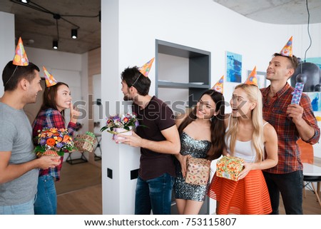 A group of people is preparing a surprise for the birthday girl. They are waiting for her with gifts. The guys and the girls are in a great mood.