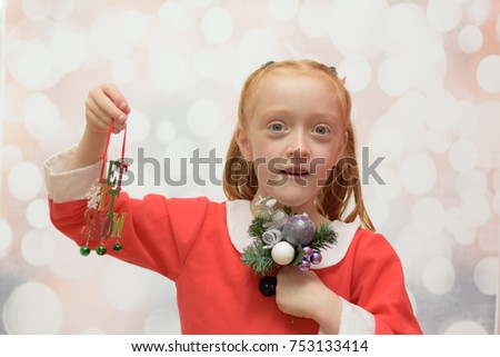 Little girl in a Santa Claus suit holding a Christmas bouquet and a Christmas decoration that reads 'let it snow' on a winter blurred background