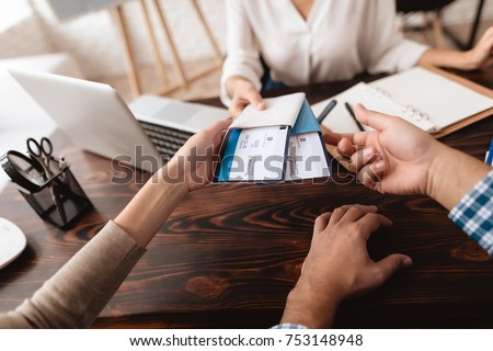 A young man and a woman came to the travel agency. They want to go on a trip during their holidays. The agent gives them tickets. Royalty-Free Stock Photo #753148948
