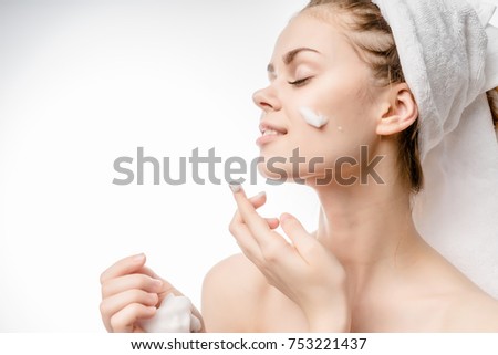 a beautiful young girl looks after her face, puts a cream on her face, on her head a white towel