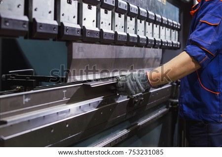 Man working with sheet metal on CNC hydraulic press brake. He puts the part and bends it into a large machine at an angle Royalty-Free Stock Photo #753231085