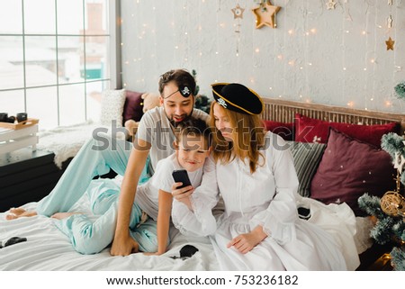 New Year's morning of a friendly family. Bedroom. Pirate style. Mom and Dad play with the child (son) in pirates. Children's games. The family is photographed on the phone (smartphone).