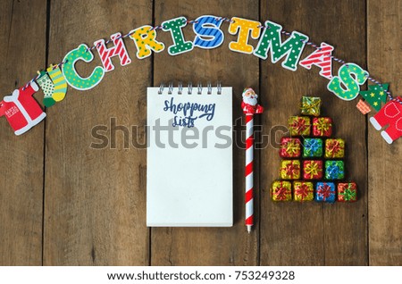 Christmas shopping background with piles of chocolate in Xmas tree shape, note, cartoon hanging on rope, Santa pen and notebook on old textured wood flat lay.   