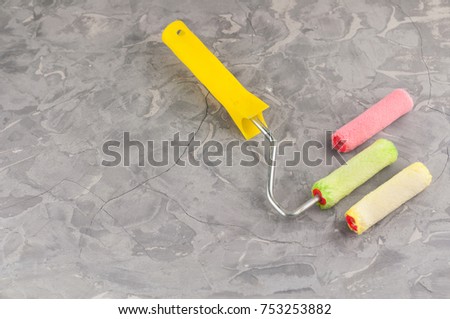Paint roller with plastic handle and two soft rolls red and yellow colors on background of gray dirty cement