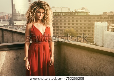 Pretty woman portrait wearing red dress on rooftop, cityscape background