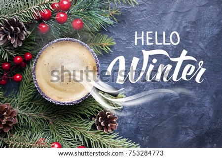 Cup of coffee cappuccino, spruce branches and cones. Great season texture with winter mood, traditional beverage for winter time. Christmas still life. Hand lettering inscription "Hello Winter"