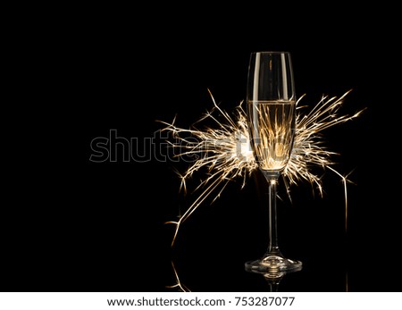Tall glass of champagne in the glow of Bengal lights. Black background. Concept of celebration and New Year.