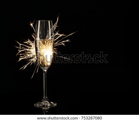 Glass of champagne in the light of bright Bengal lights. Black background. Concept of celebration and New Year.