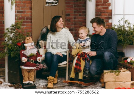 Young happy parents with a cute little child boy on rocking horse, dressed in sweater in decorated New Year room with Santa at home. Christmas good mood. Lifestyle, family and holiday 2018 concept.