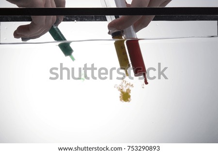 syringe with paint in water, waves of colors in water